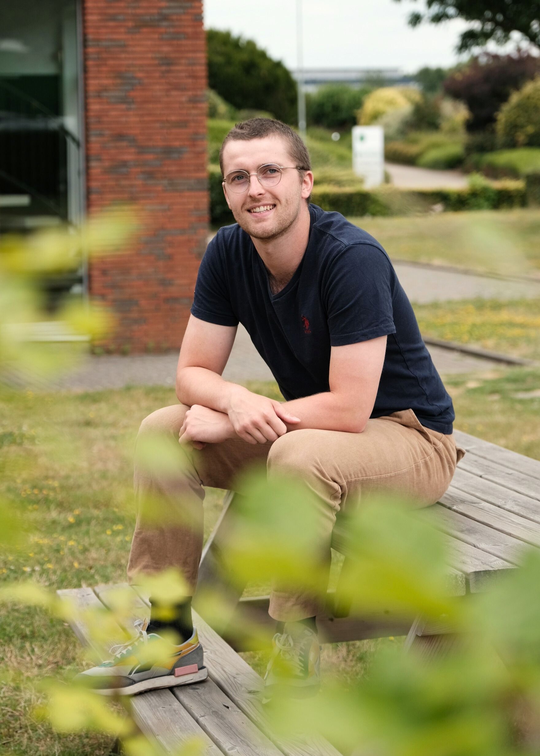 Man met kort, bruin haar en een lichtgrijze dunne bril zit op een picknicktafel en lacht naar de camera