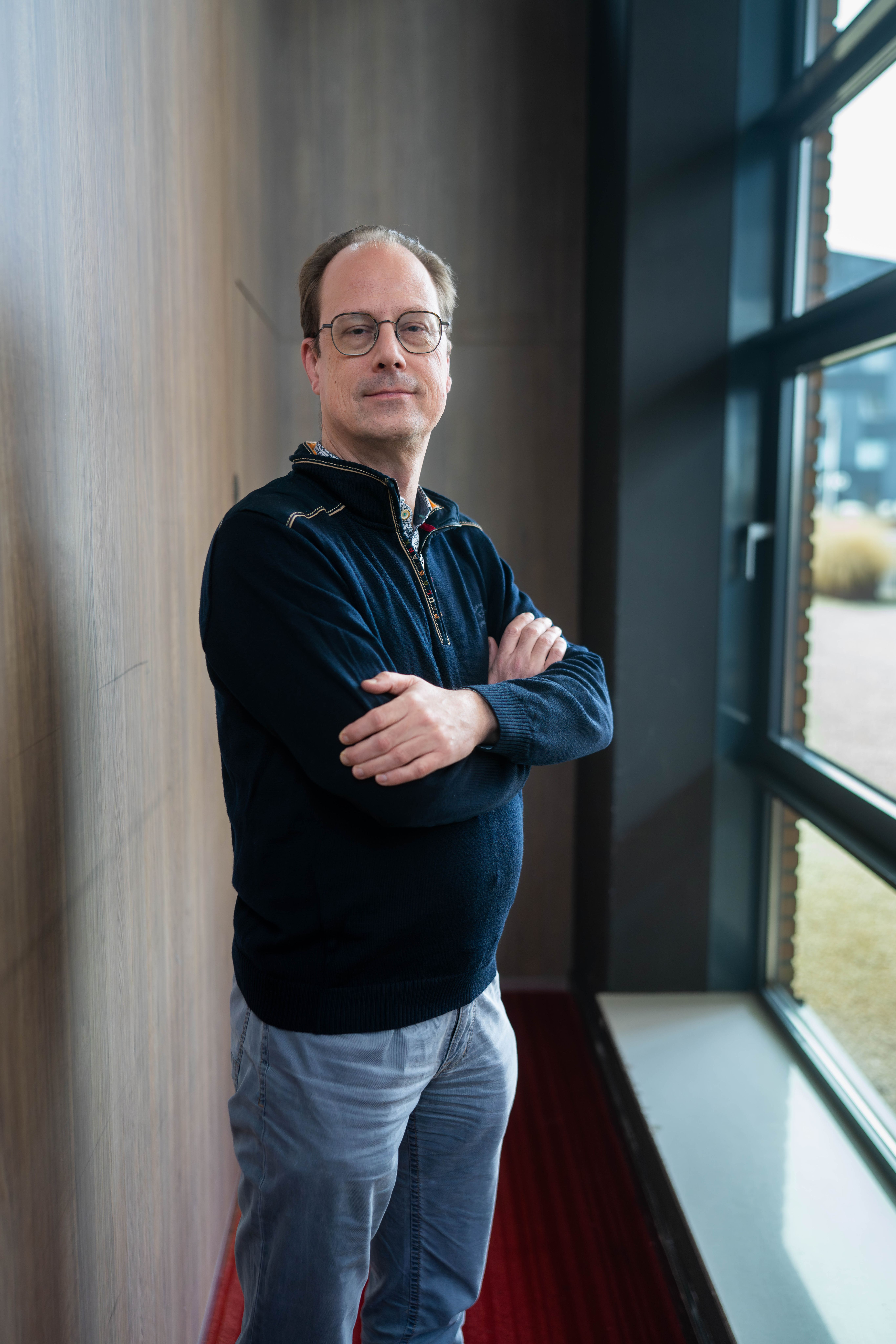 Man met armen over elkaar, blauwe trui, blauwe spijkerbroek