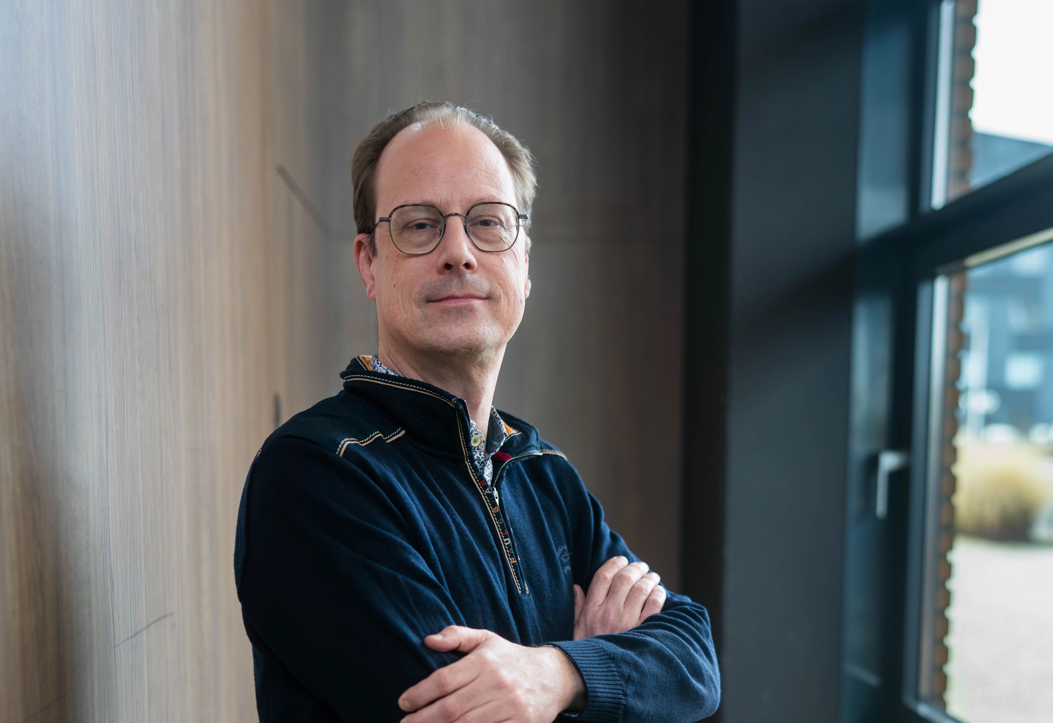 Man met armen over elkaar, blauwe trui, blauwe spijkerbroek