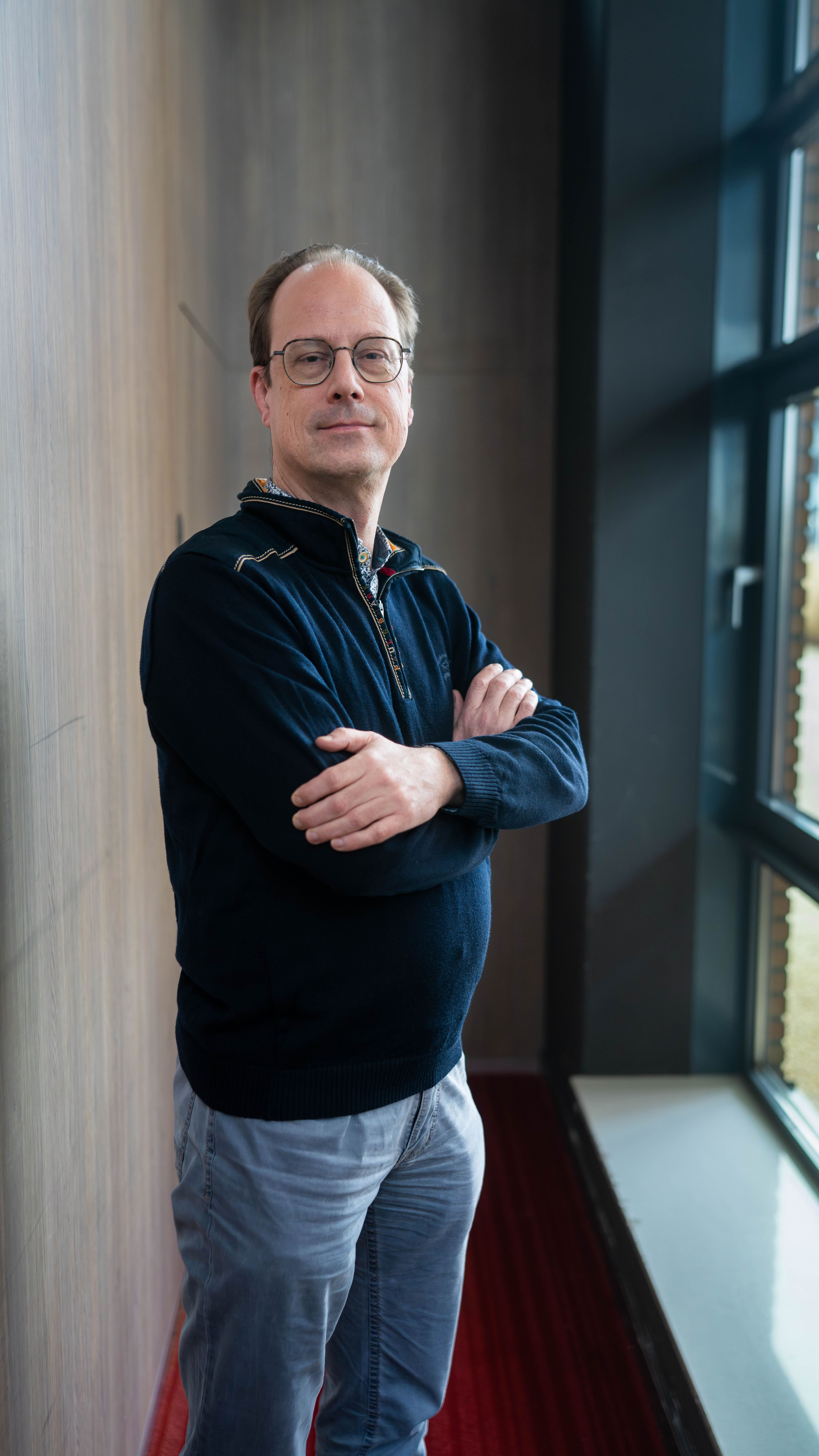 Man met armen over elkaar, blauwe trui, blauwe spijkerbroek