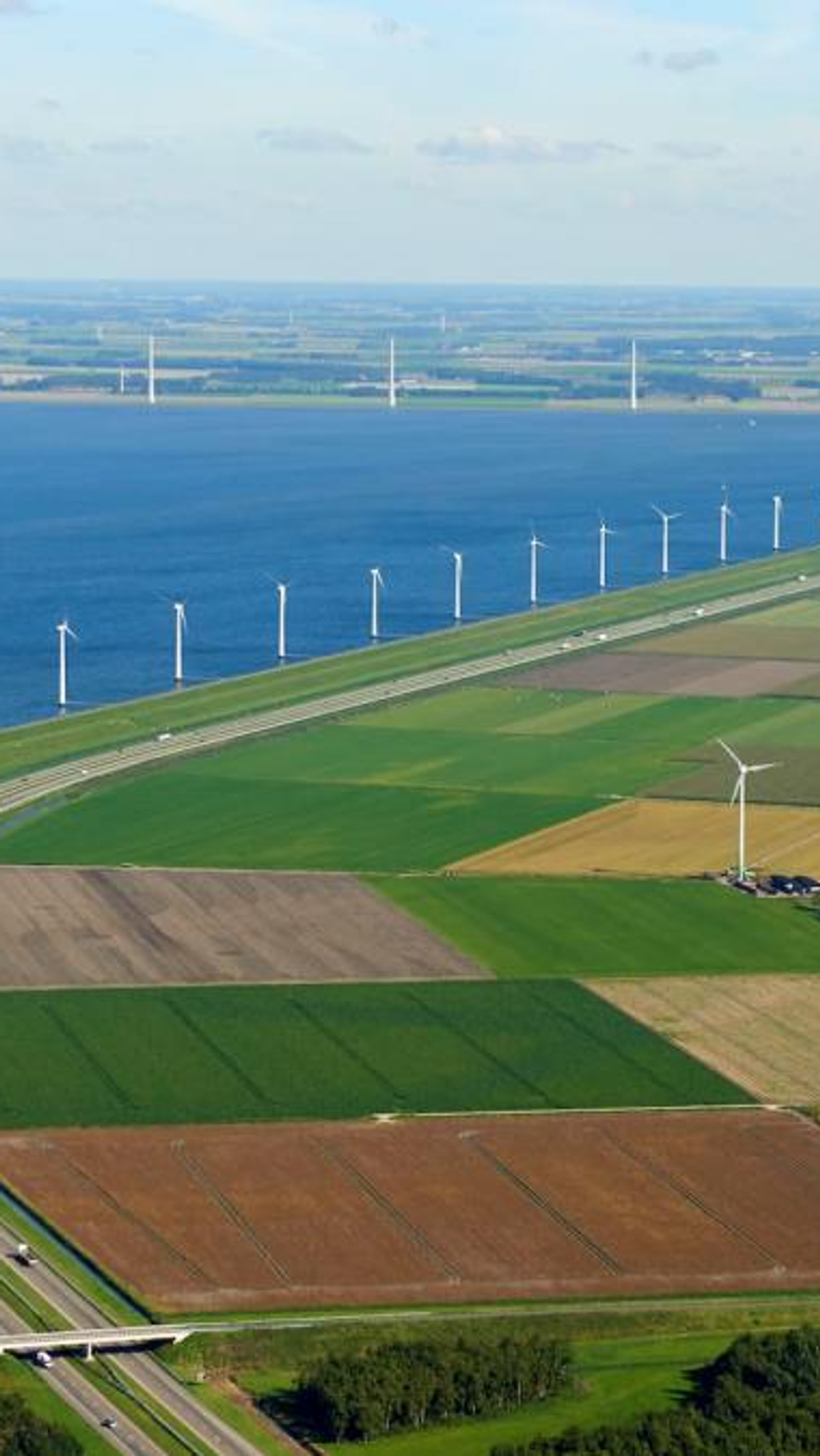 Luchtfoto van dijk langs IJsselmeer met windmolens en agrarisch land