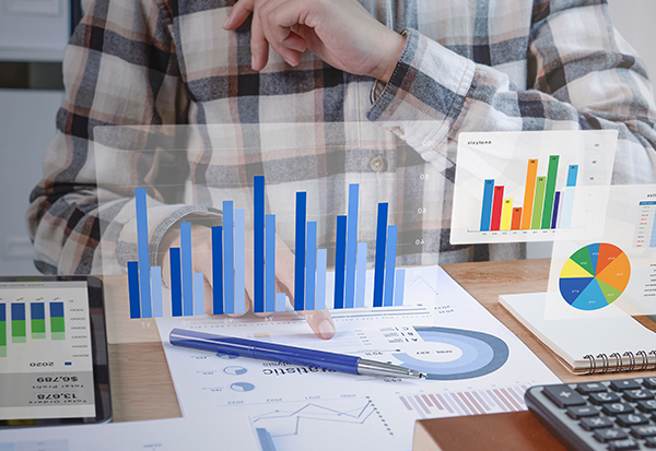 Persoon in geruit overhemd analyseert grafieken en dashboards met financiële data op papier, tablet en holografische visualisaties.
