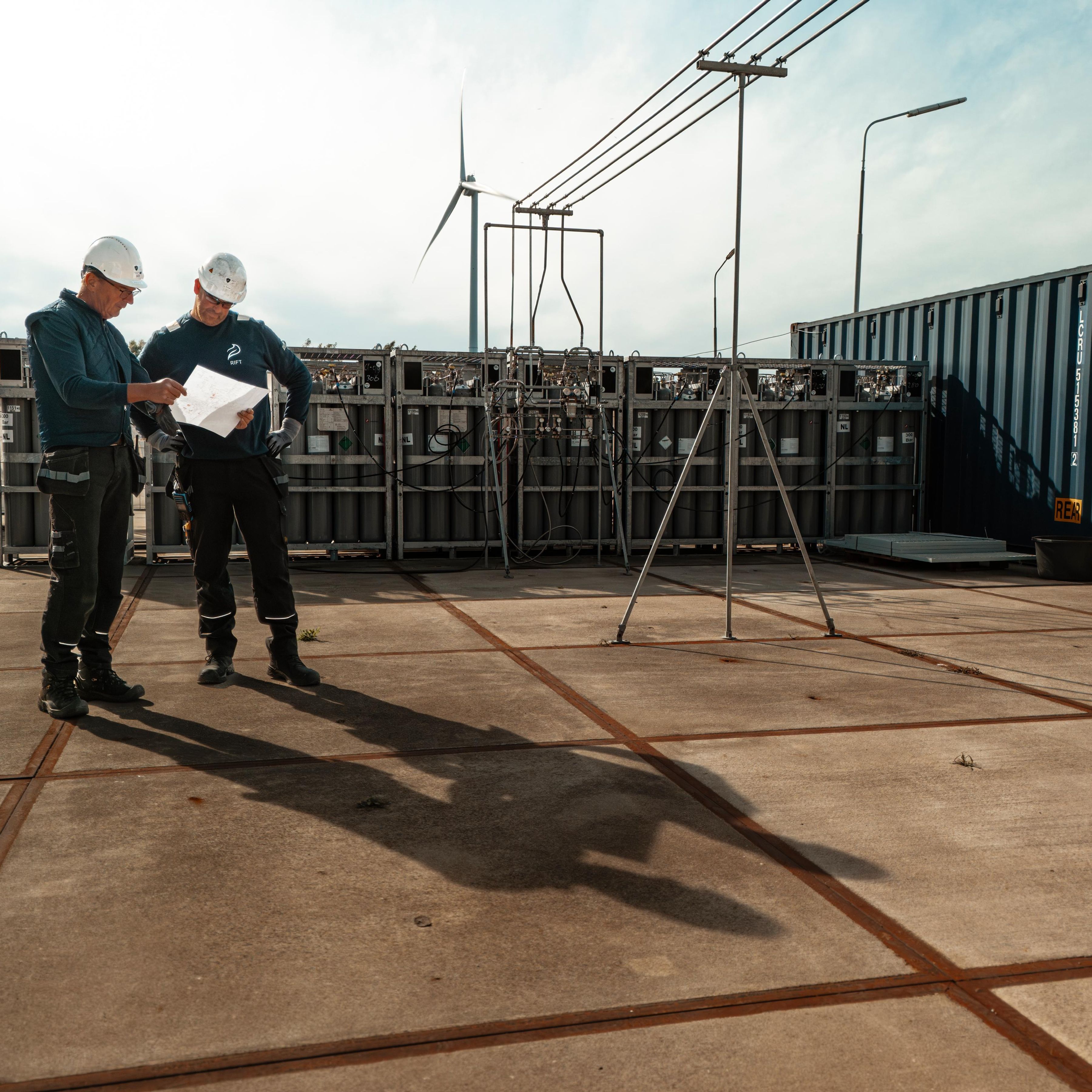 Two men in hard hats inspect a construction document