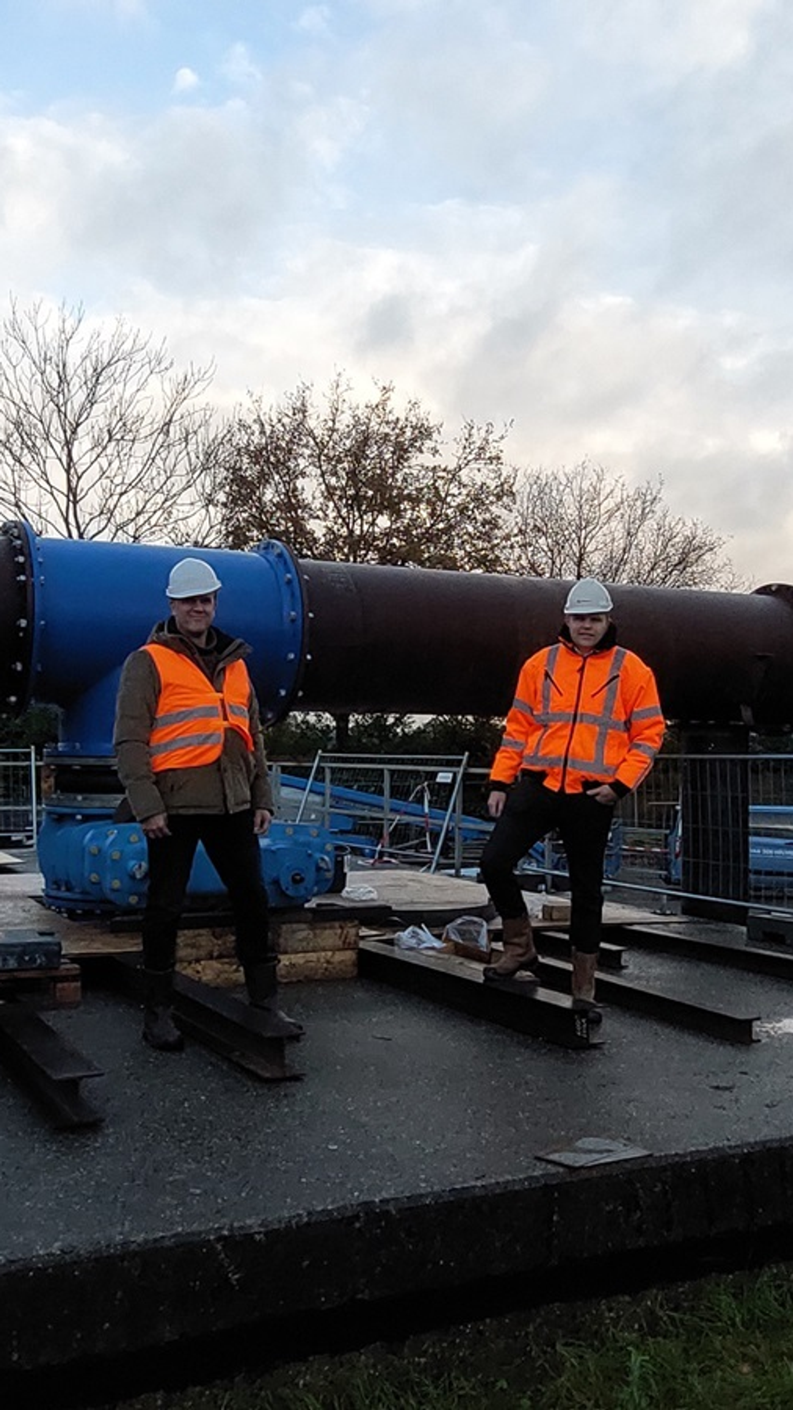 Twee werknemers in veiligheidspakken bij grote blauwe leidinginstallatie