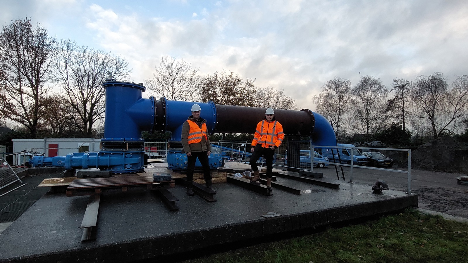 Twee werknemers in veiligheidspakken bij grote blauwe leidinginstallatie