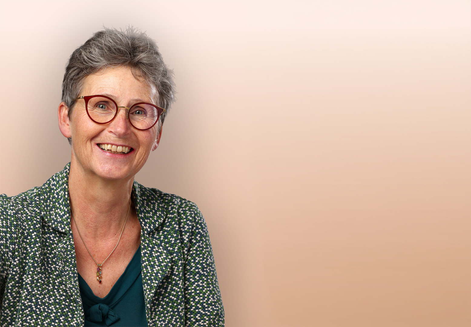Vrouw met grijs haar en een rode bril lacht vriendelijk naar de camera
