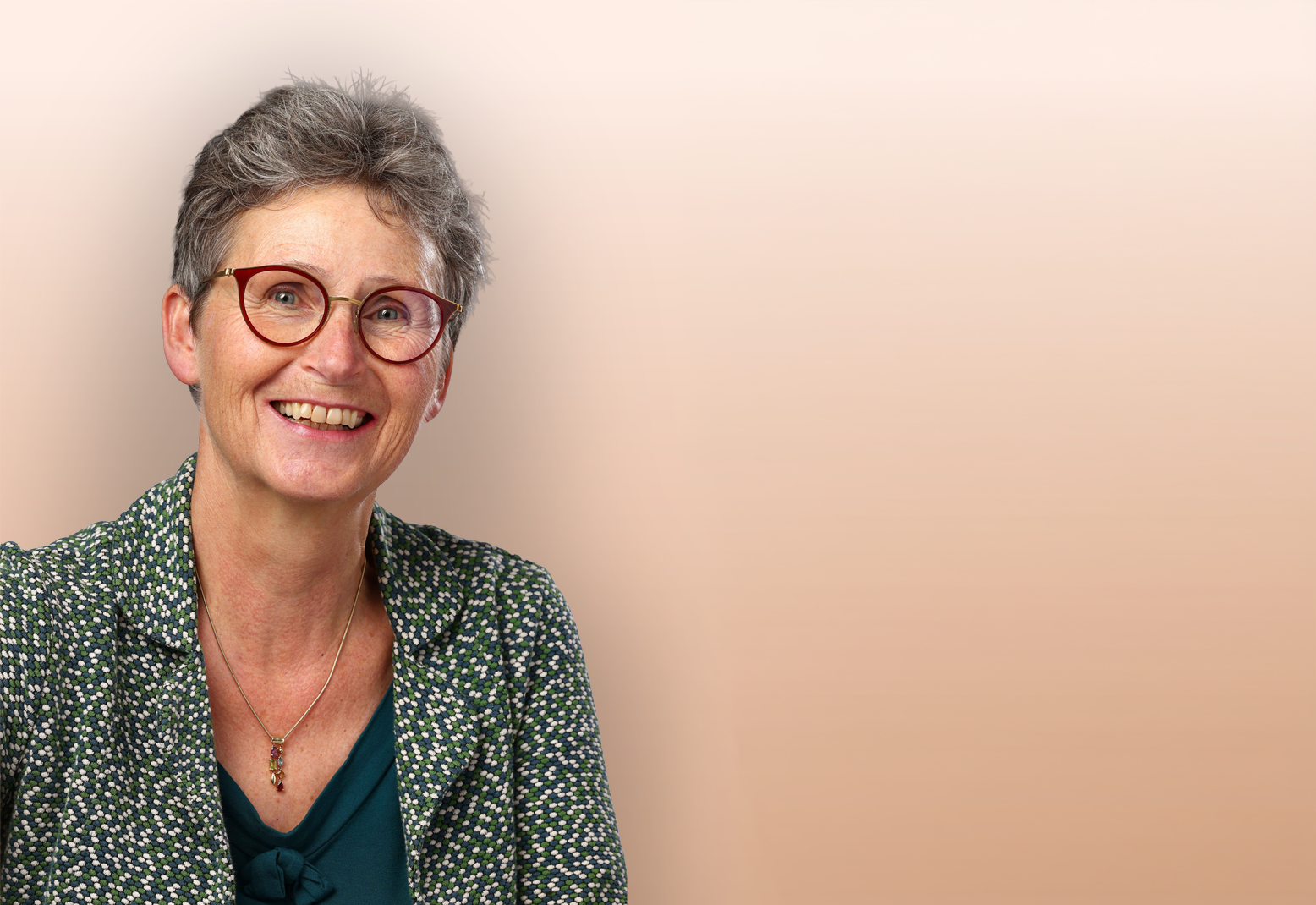 Vrouw met grijs haar en een rode bril lacht vriendelijk naar de camera