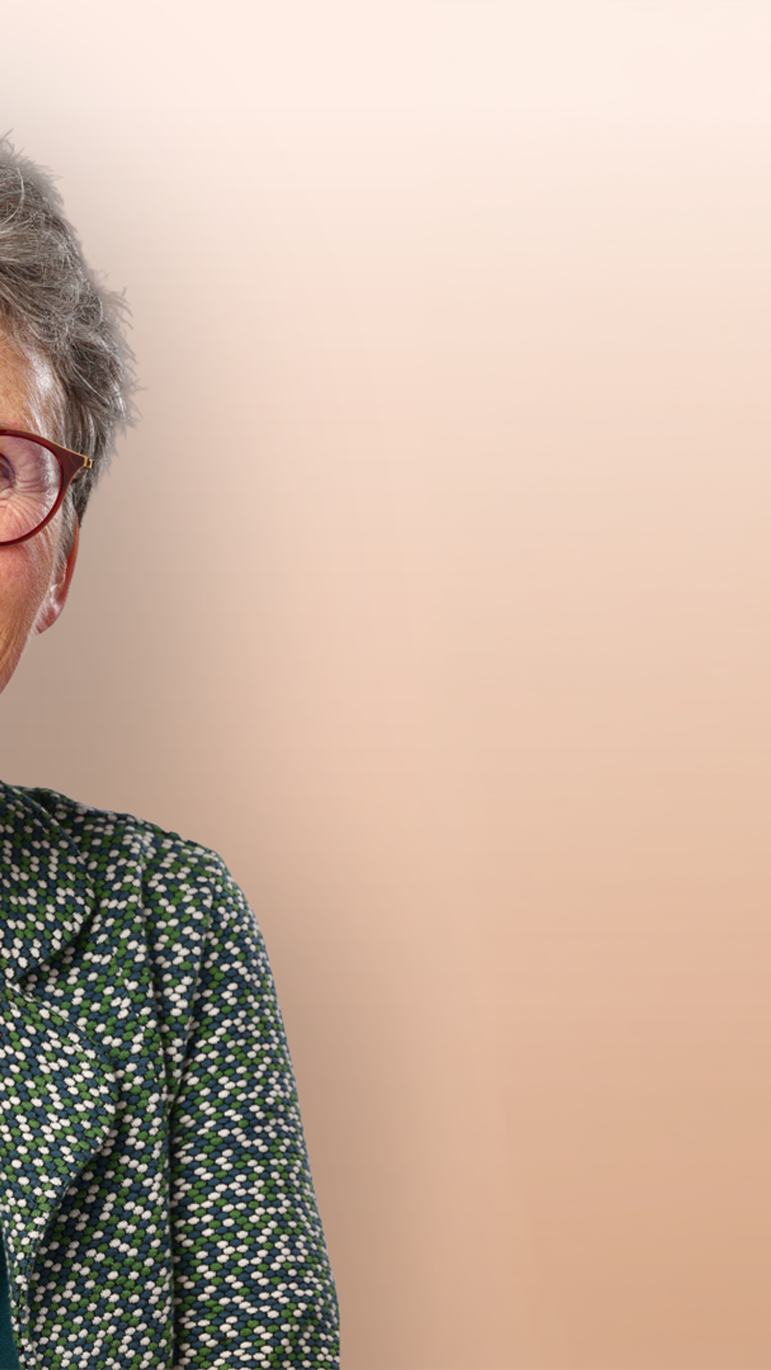 Vrouw met grijs haar en een rode bril lacht vriendelijk naar de camera