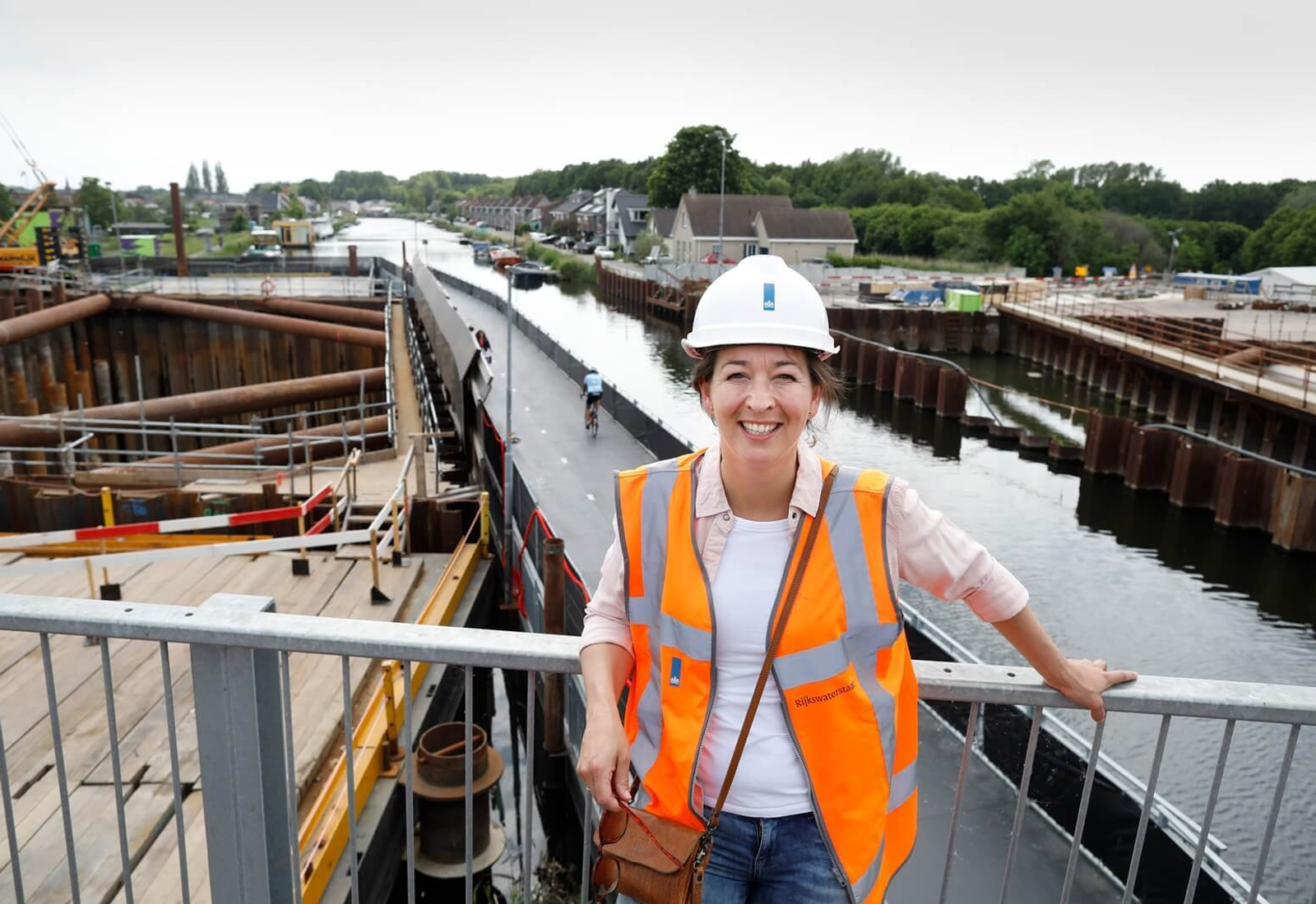 Omgevingsadviseur Nienke in veiligheidshesje en helm op een bouwlocatie van de A16 Rotterdam, met zicht op werkzaamheden langs het water.
