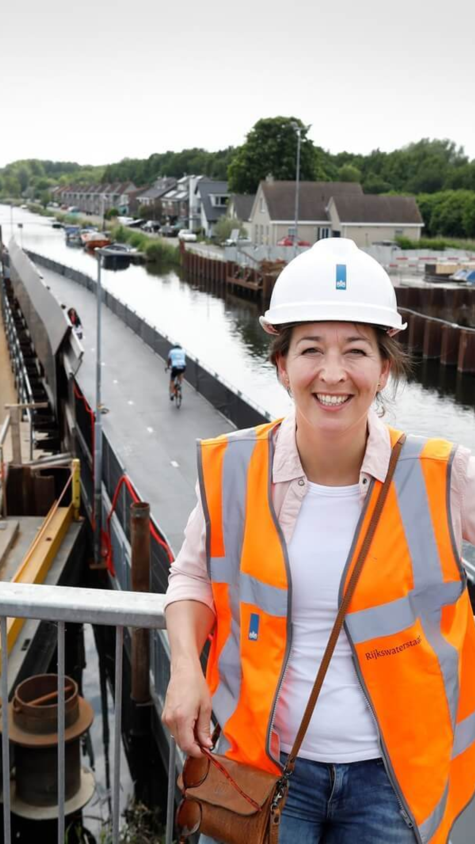 Omgevingsadviseur Nienke in veiligheidshesje en helm op een bouwlocatie van de A16 Rotterdam, met zicht op werkzaamheden langs het water.