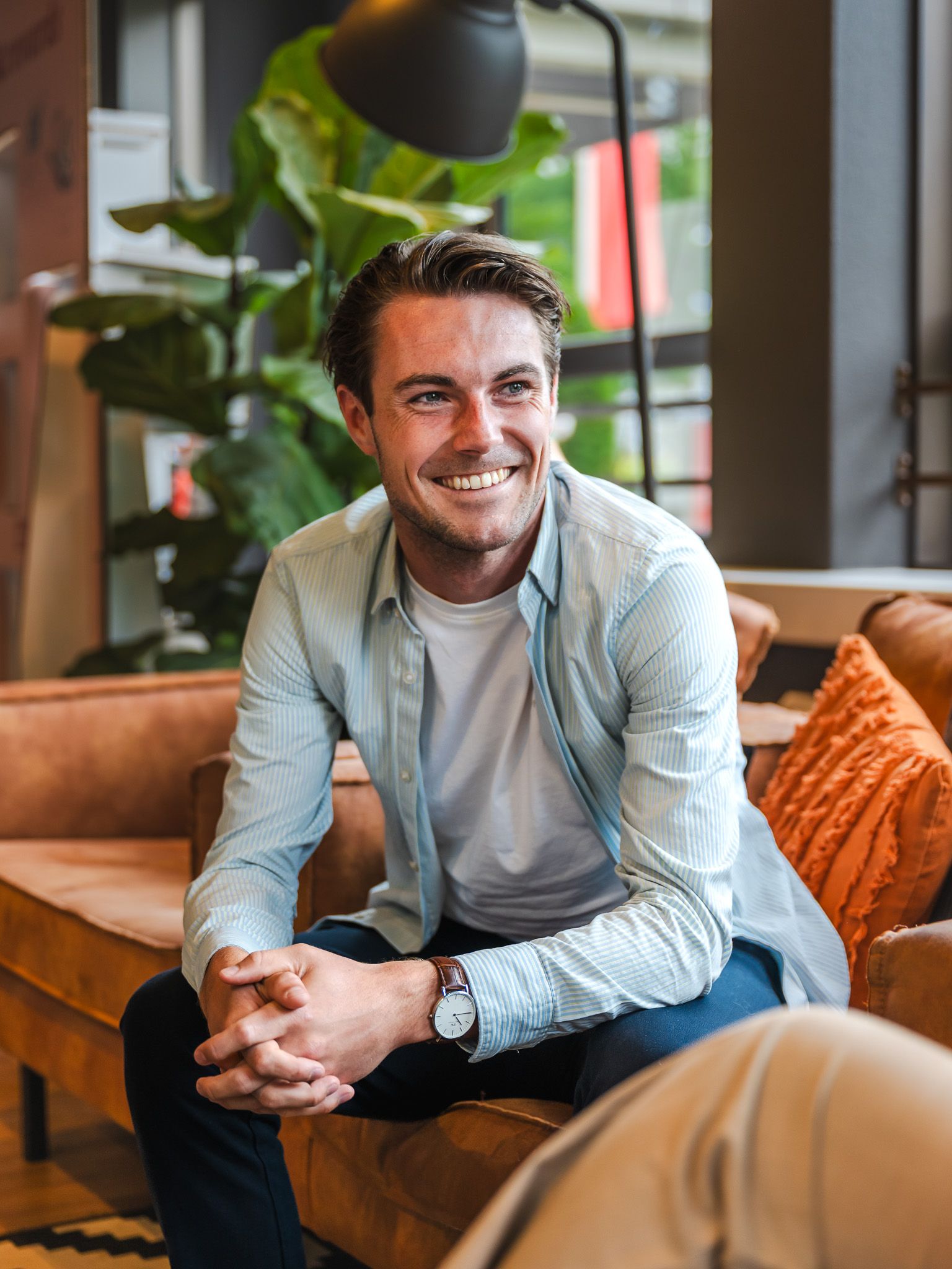 Man met bruin haar, lachend op een oranje bank