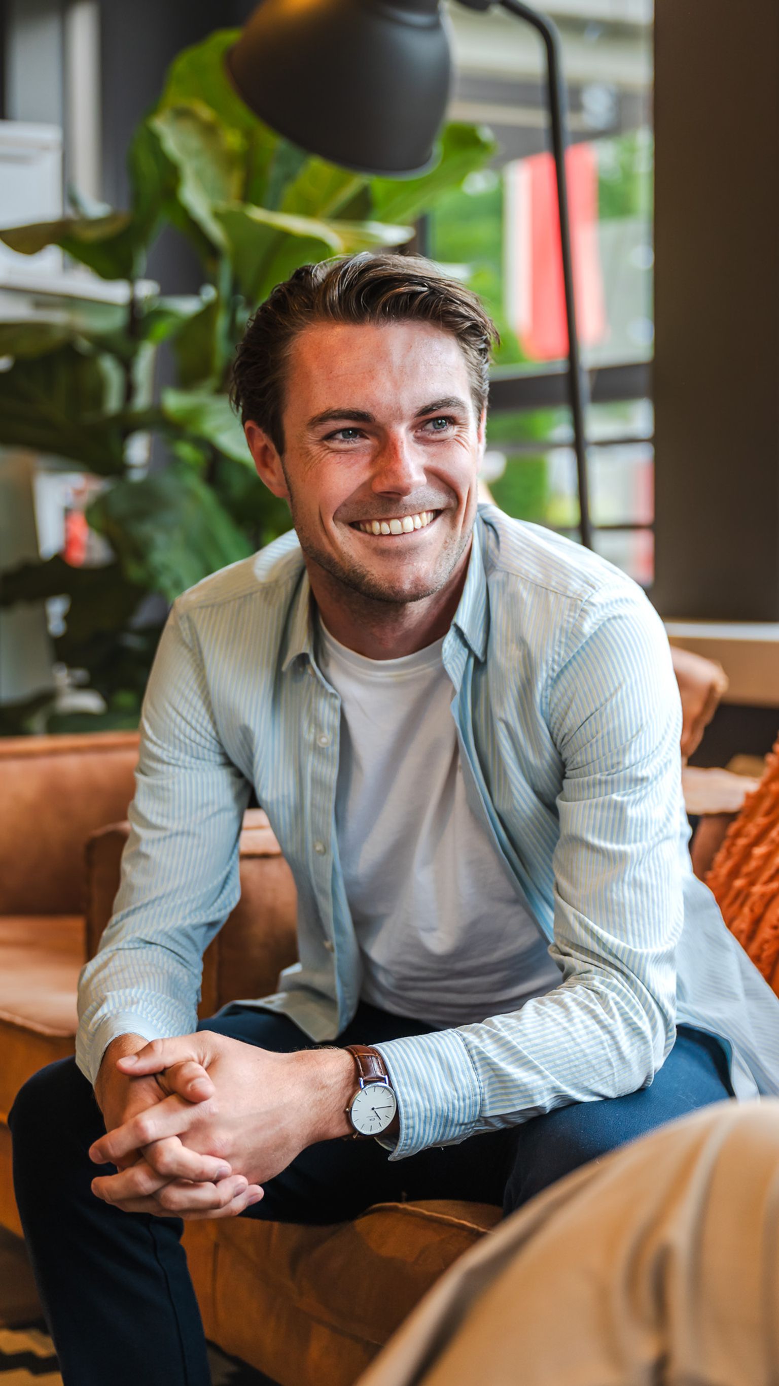 Man met bruin haar, lachend op een oranje bank