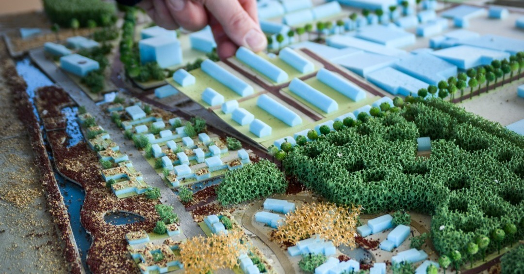 Hand plaatst gebouw op architectuurmaquette met groene landschapselementen