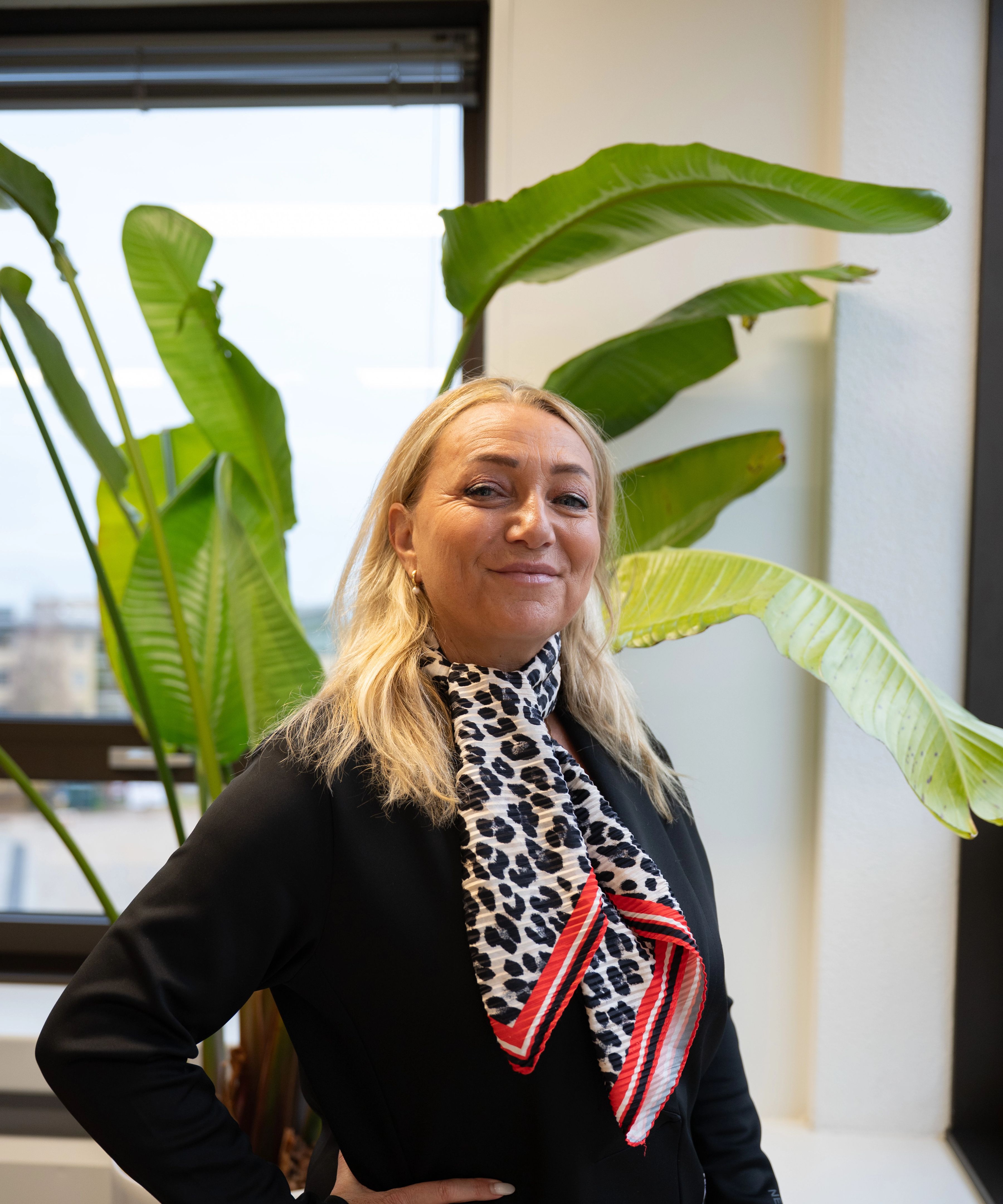 Blonde vrouw lacht naar de camera, ze draagt een zwarte colbert en een panterprint sjaaltje.