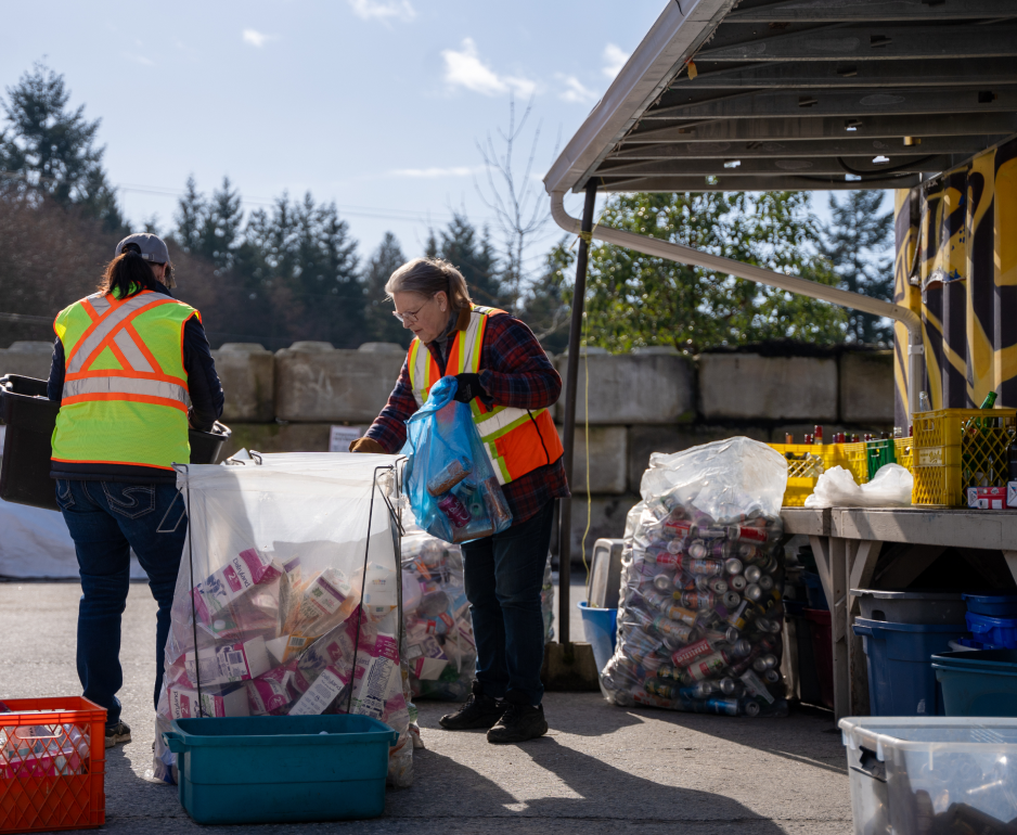 Two people in high-visibility vests sort recycling into various bags.