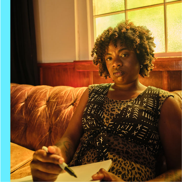 A person sitting on a couch holding a pen and a notebook.