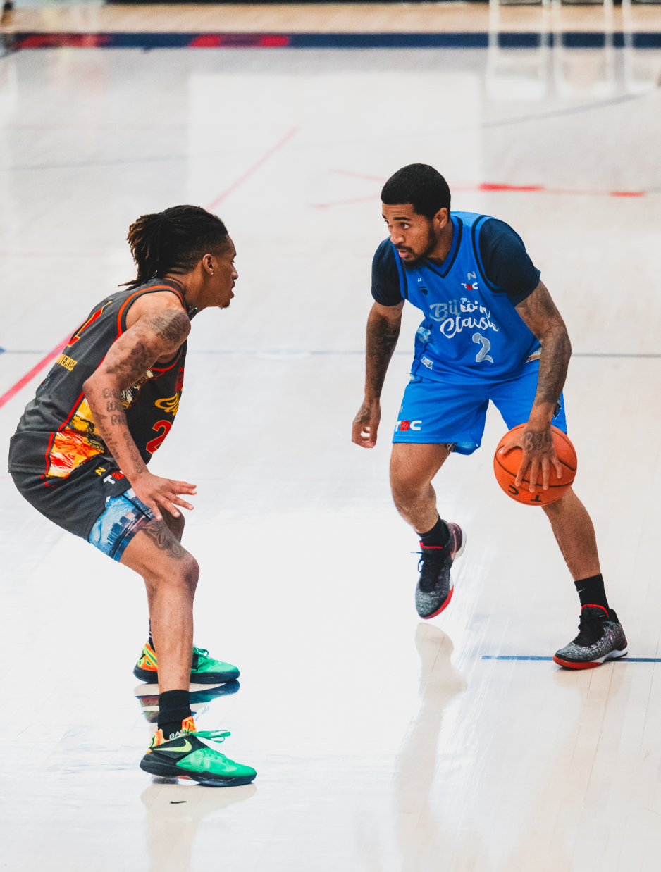 Two people play basketball on an indoor court.
