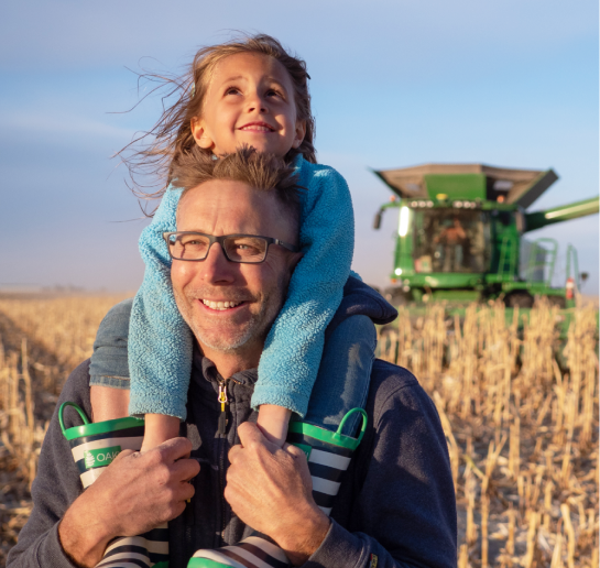 A person carrying a child on his shoulders in a crop field.