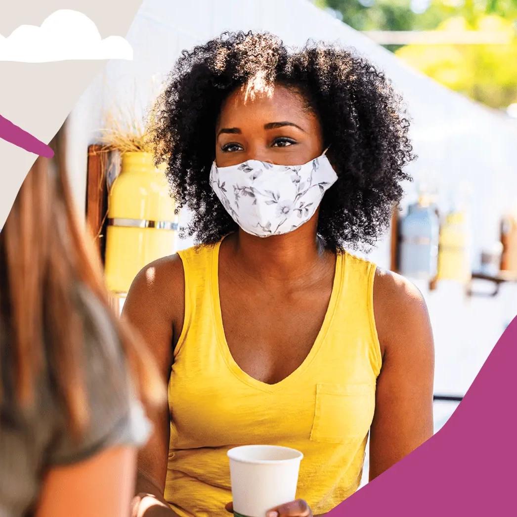 A person standing outside wearing a face mask, holding a paper cup.
