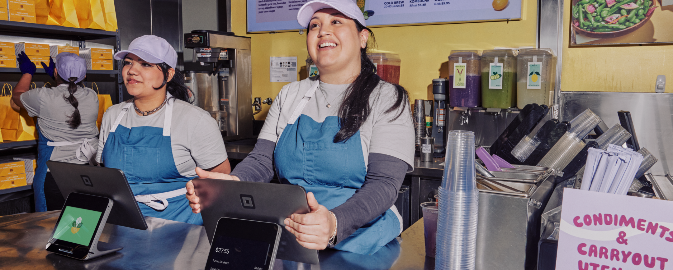 Two smiling restaurant cashiers ringing up customers using Square Stands.