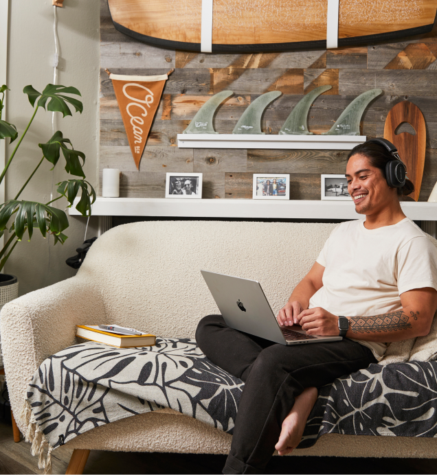 A person sitting on a couch with headphones on looking at a laptop.