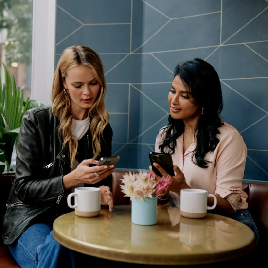 Two women sitting at a table looking at their phones.