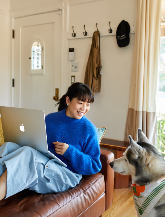 A person sitting in a chair with a dog looking at a laptop