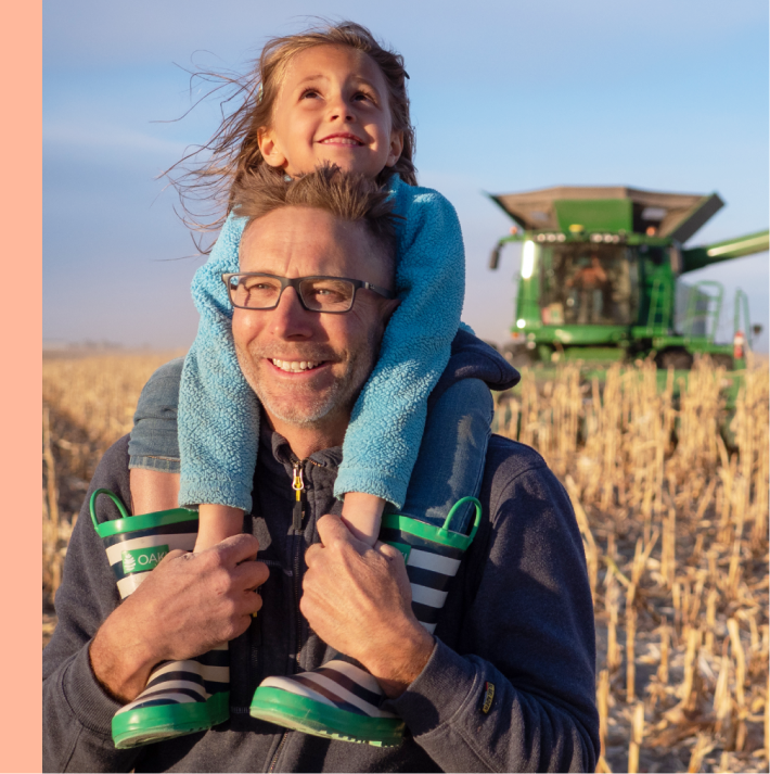 A person carrying a child on his shoulders in a crop field.