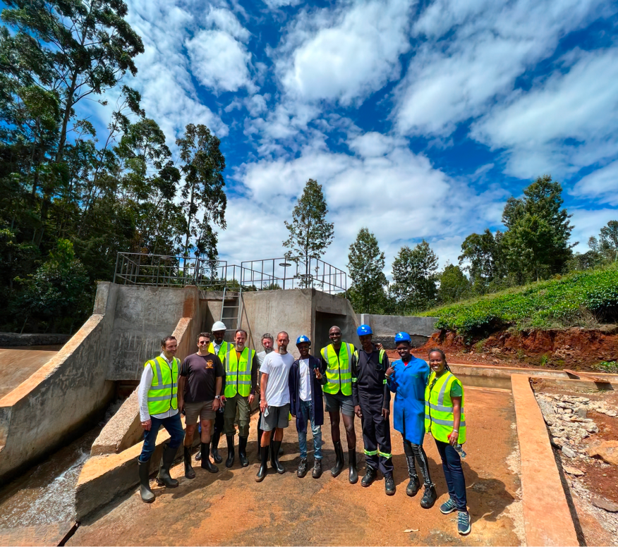 A group of men in safety vests and helmets standing in front of a concrete dam.
