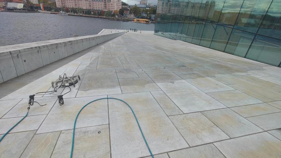 Rengjøring av hvit marmor på taket av Operahuset i Oslo, med høytrykksutstyr og slange på flaten og fjorden i bakgrunnen
