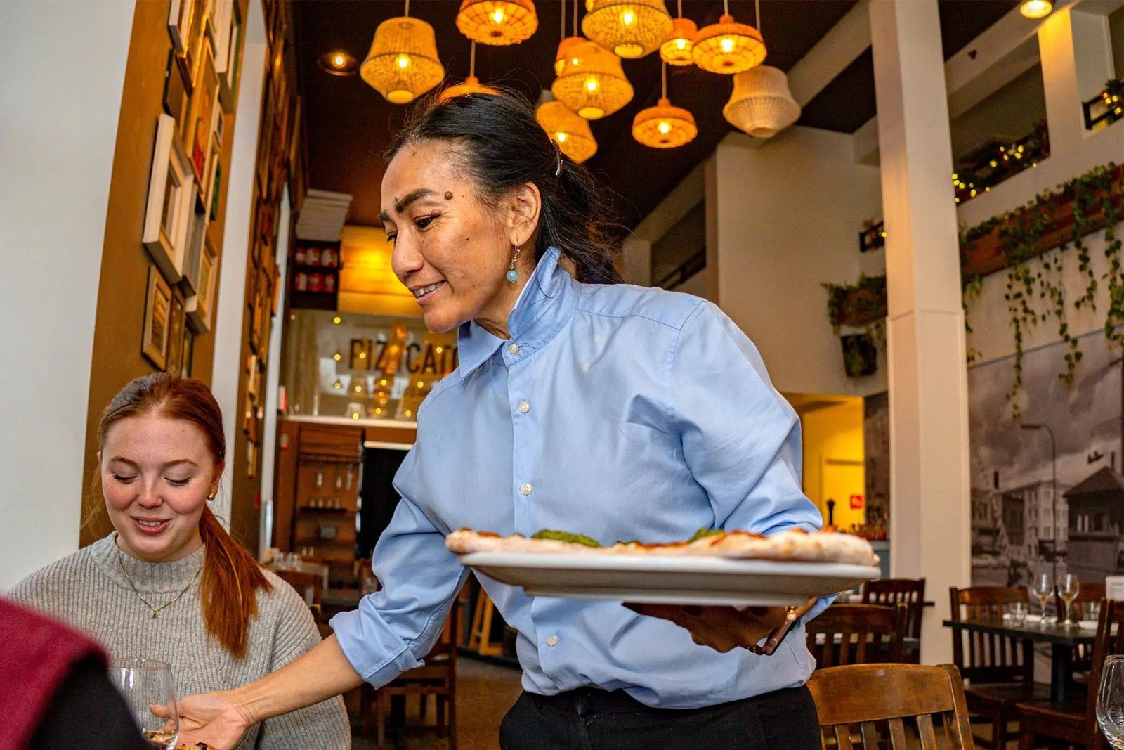 Une serveuse apporte une pizza à une table de Pizzicato