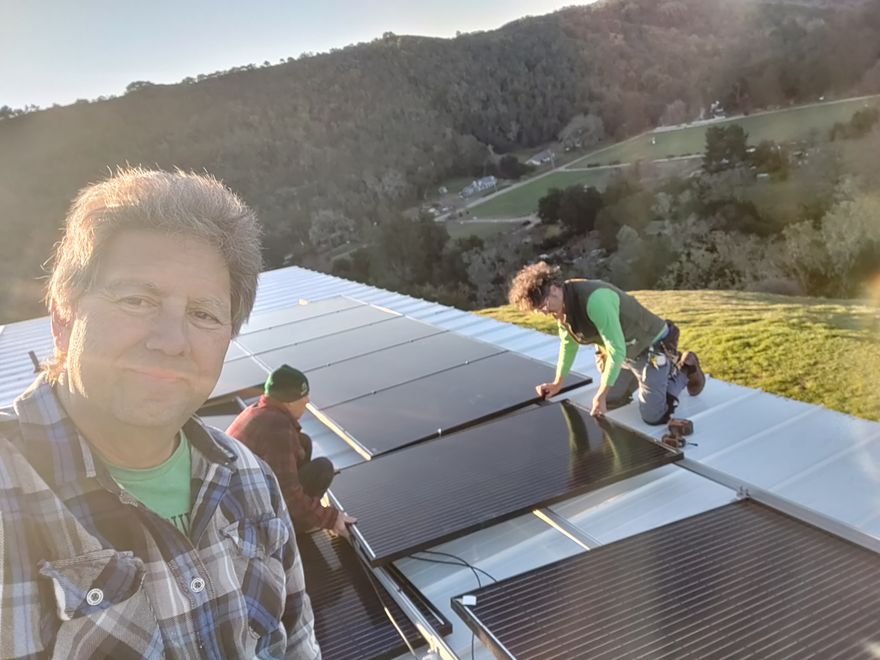 A homeowner and two helpers installing black solar panels on a metal roof.
