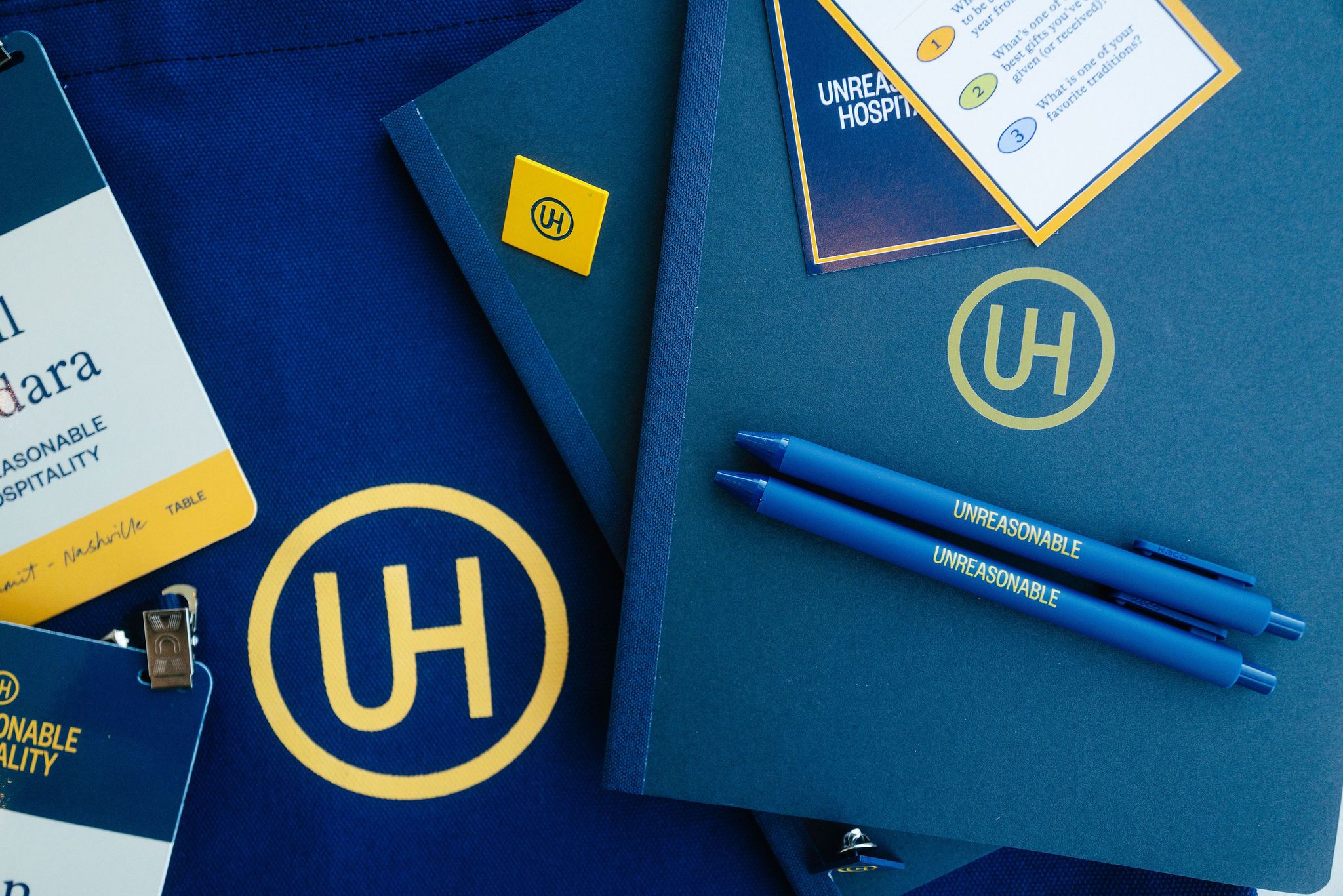 Materials at the Unreasonable Hospitality Summit: pens, badges, notebook, pin, and conversation cards