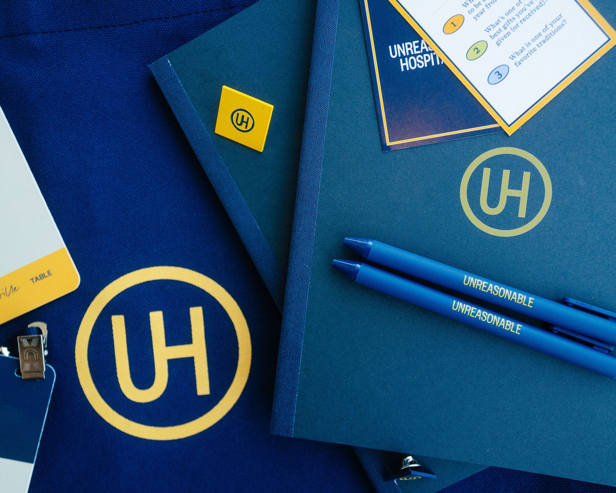Materials at the Unreasonable Hospitality Summit: pens, badges, notebook, pin, and conversation cards