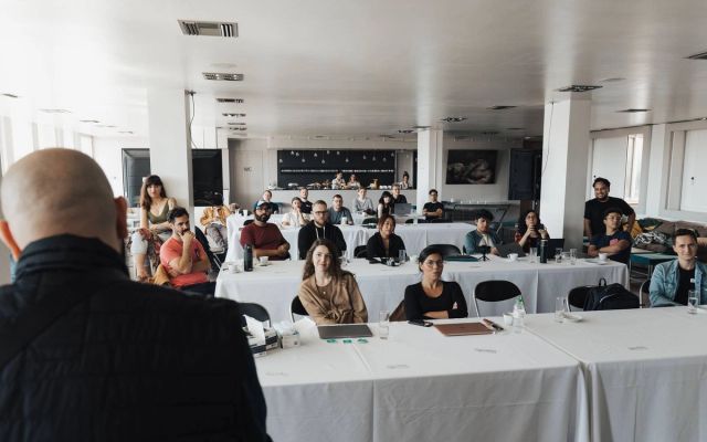 A workshop room with people working at laptops around a table.