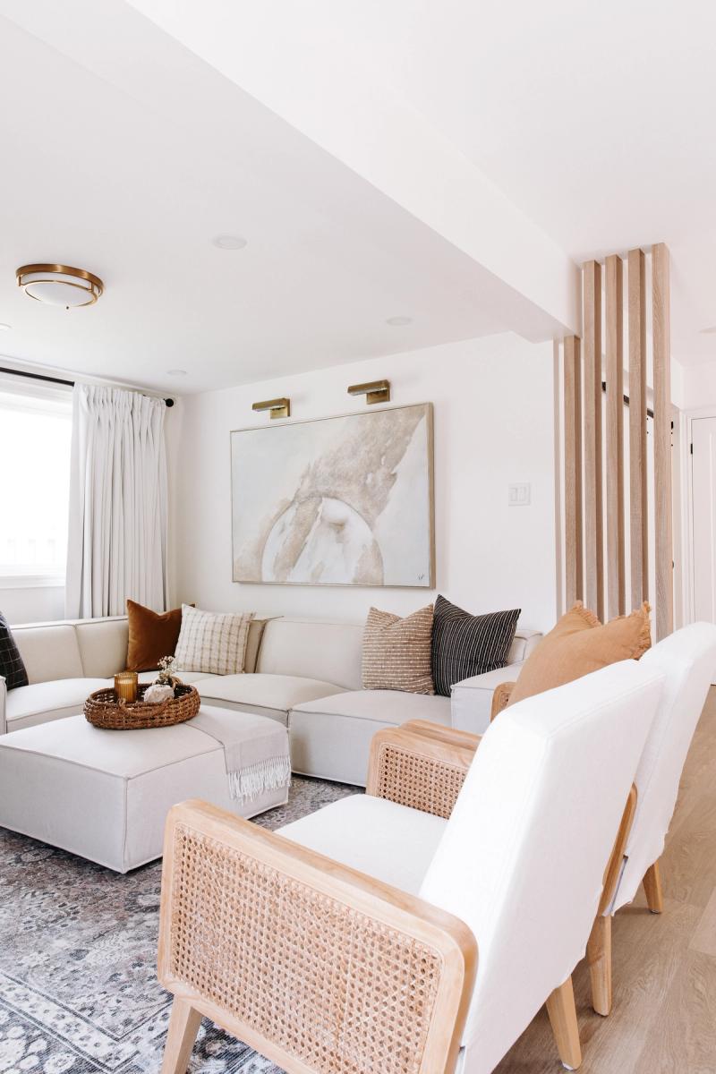 A white sectional and two cane armchairs, a painting on the wall behind