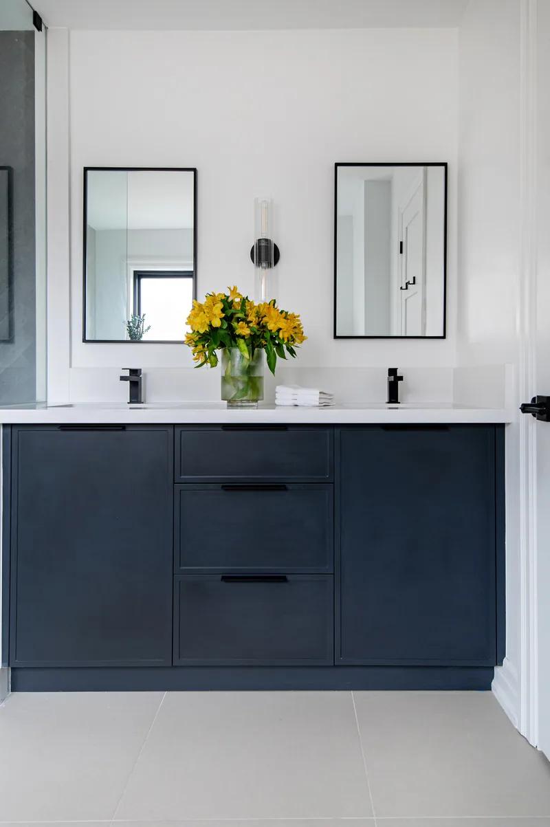 A navy double vanity under two black-framed mirrors