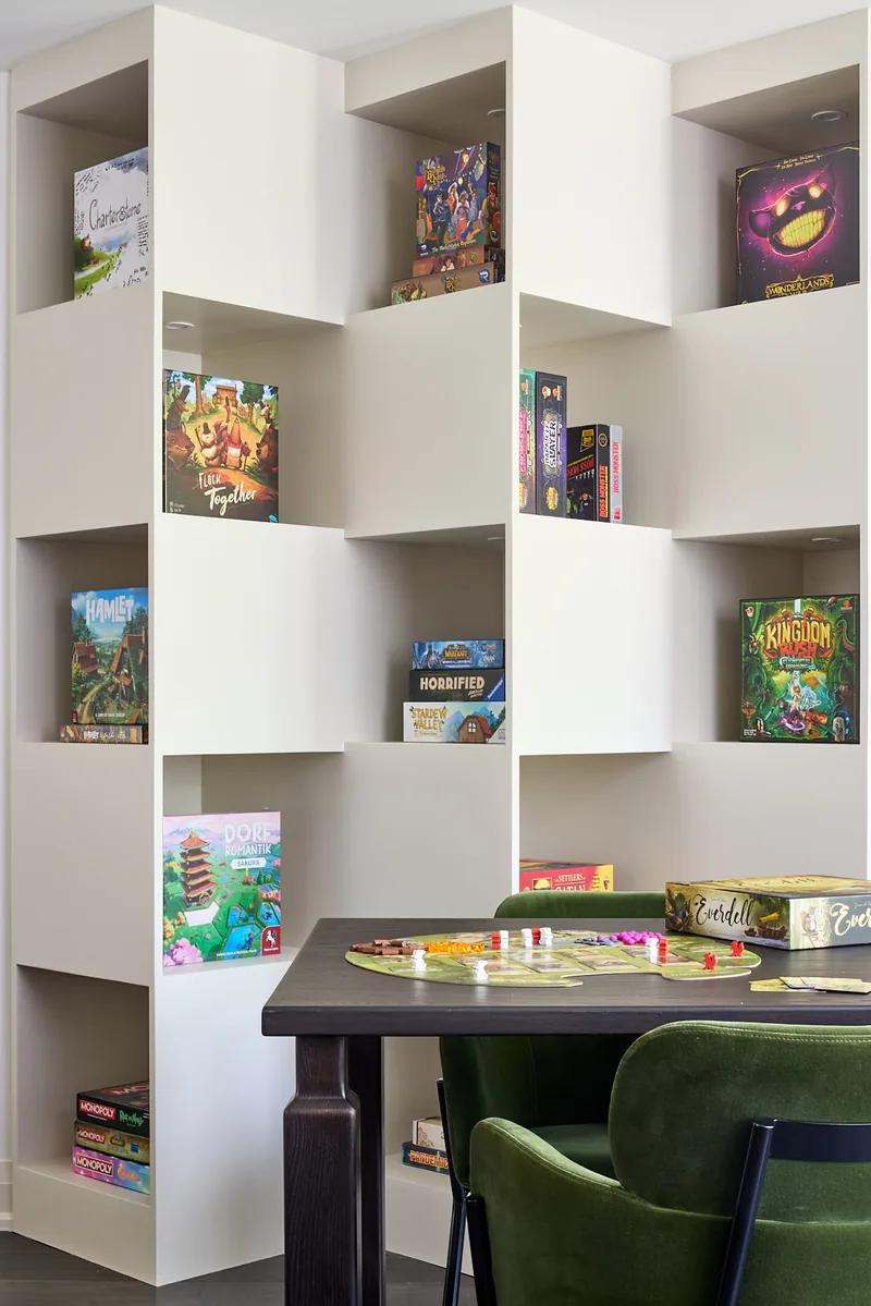 A wall of white shelving built to hold a games collection, a dining table in front