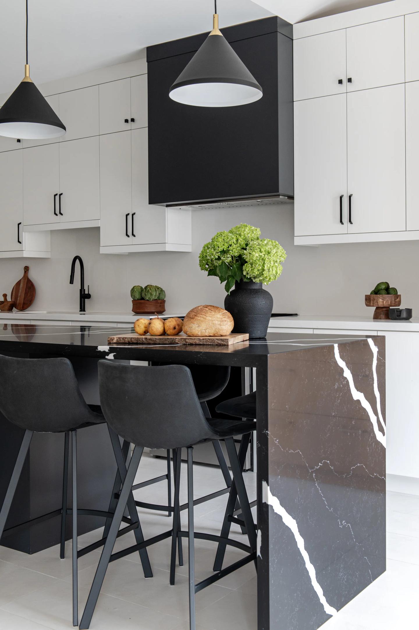 A kitchen island in black marble with a waterfall end, under black pendants