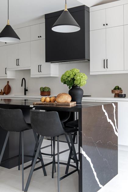A kitchen island in black marble with a waterfall end, under black pendants