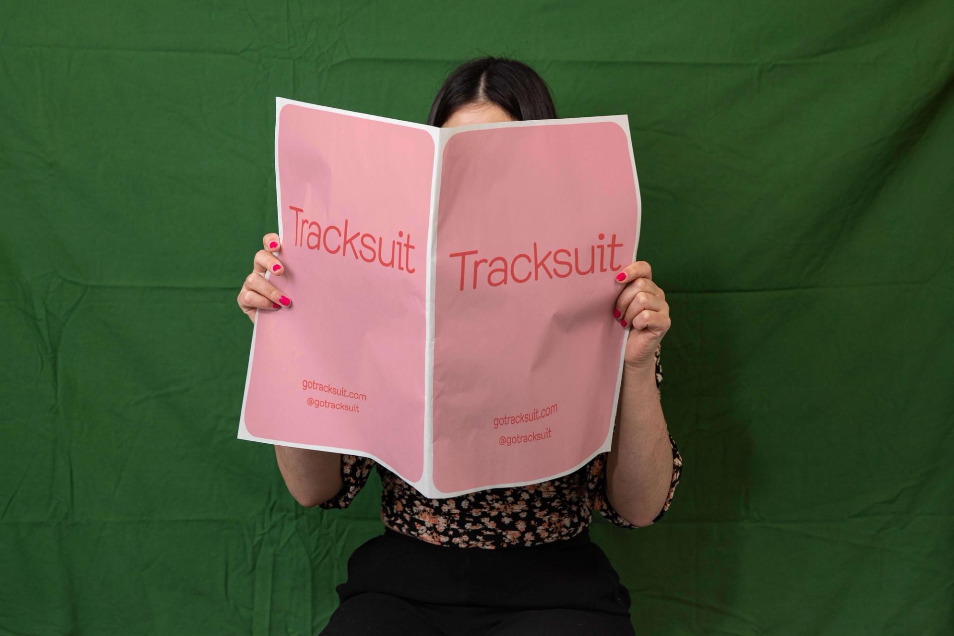Woman holding a pink book in front of her face with tracksuit branding
