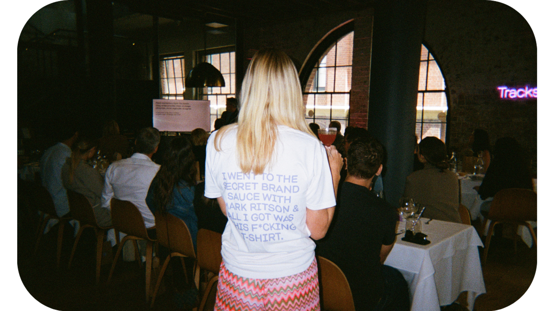 A woman wearing a t-shirt that says 'I went to the secret brand sauce with Mark Ritson', symbolizing her attendance at a marketing event where Mark Ritson shared insights on brand strategy and marketing