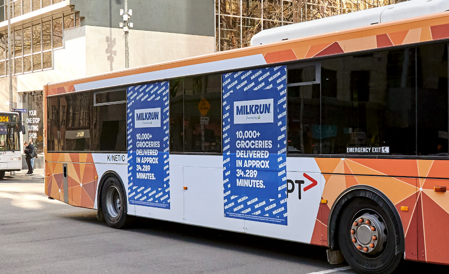 A pink bus displaying an advertisement for MILKRUN, an ultra-fast grocery delivery service in Australia, promoting brand awareness and customer acquisition.