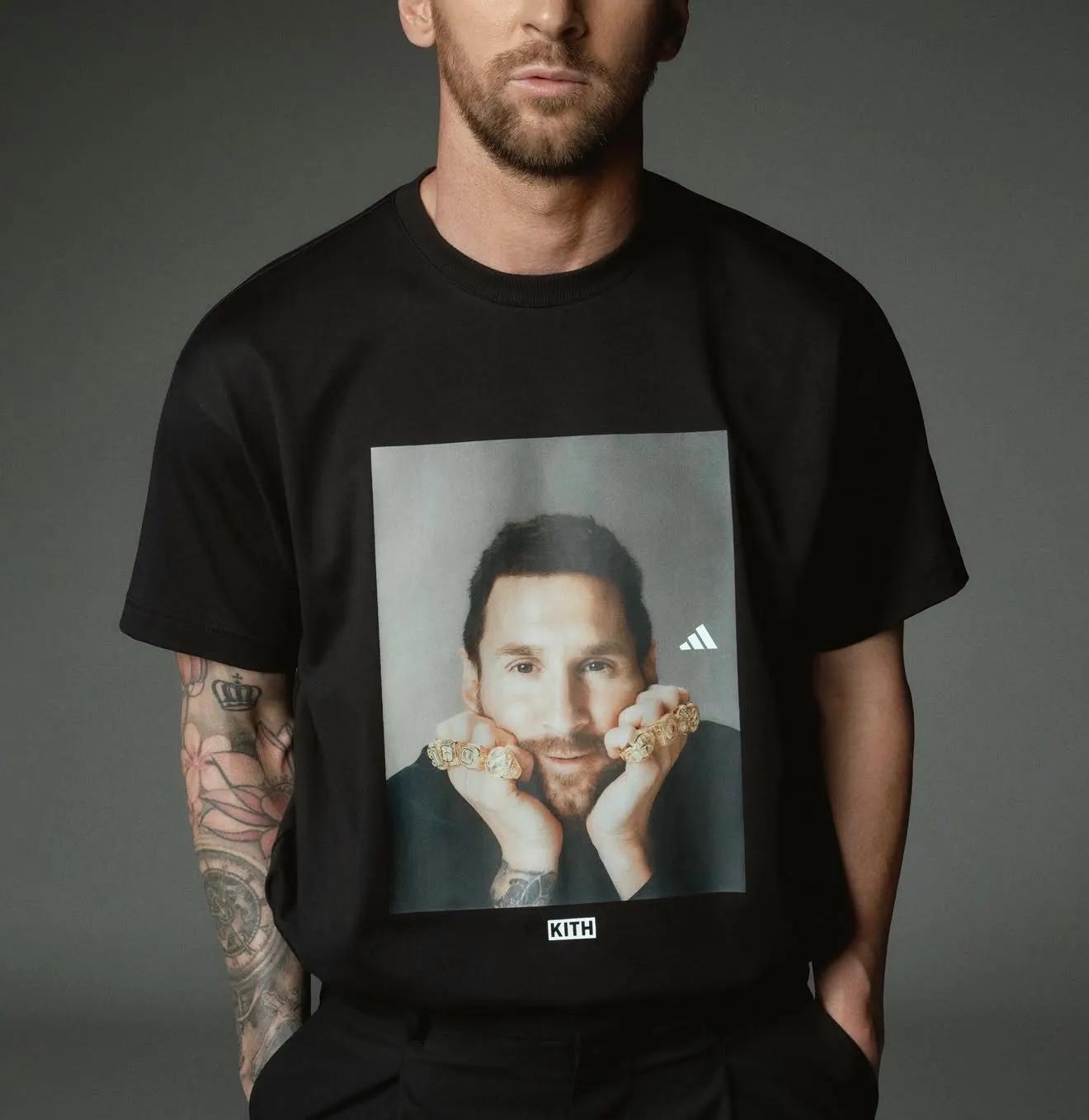 A person wearing a black KITH x Adidas t-shirt with a graphic of Lionel Messi wearing gold rings.