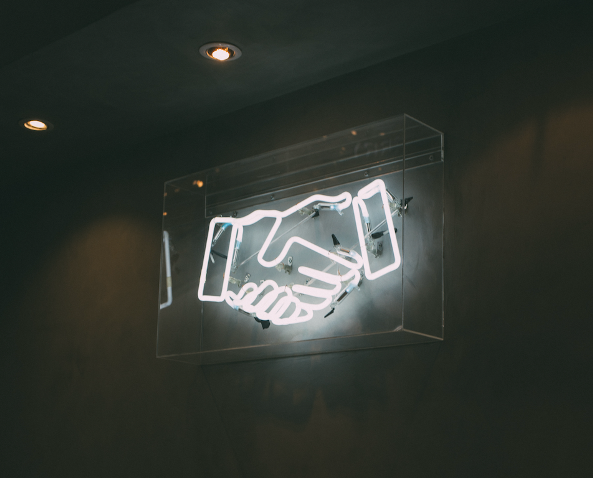 A neon sign of a handshake is lit up on a wall