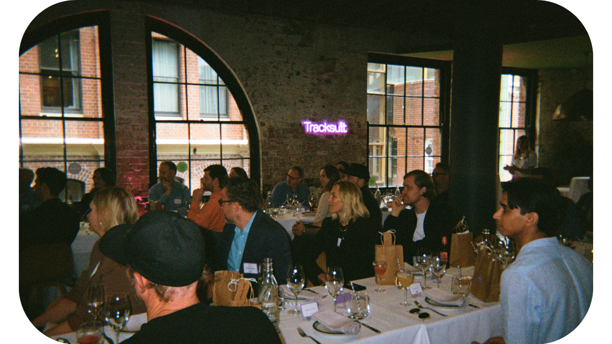 A group of people engaged in a discussion at tables, with a neon sign displaying the word 'Tracksuit' in the background. The image is from a marketing event where Mark Ritson shared insights on brand strategy and marketing.