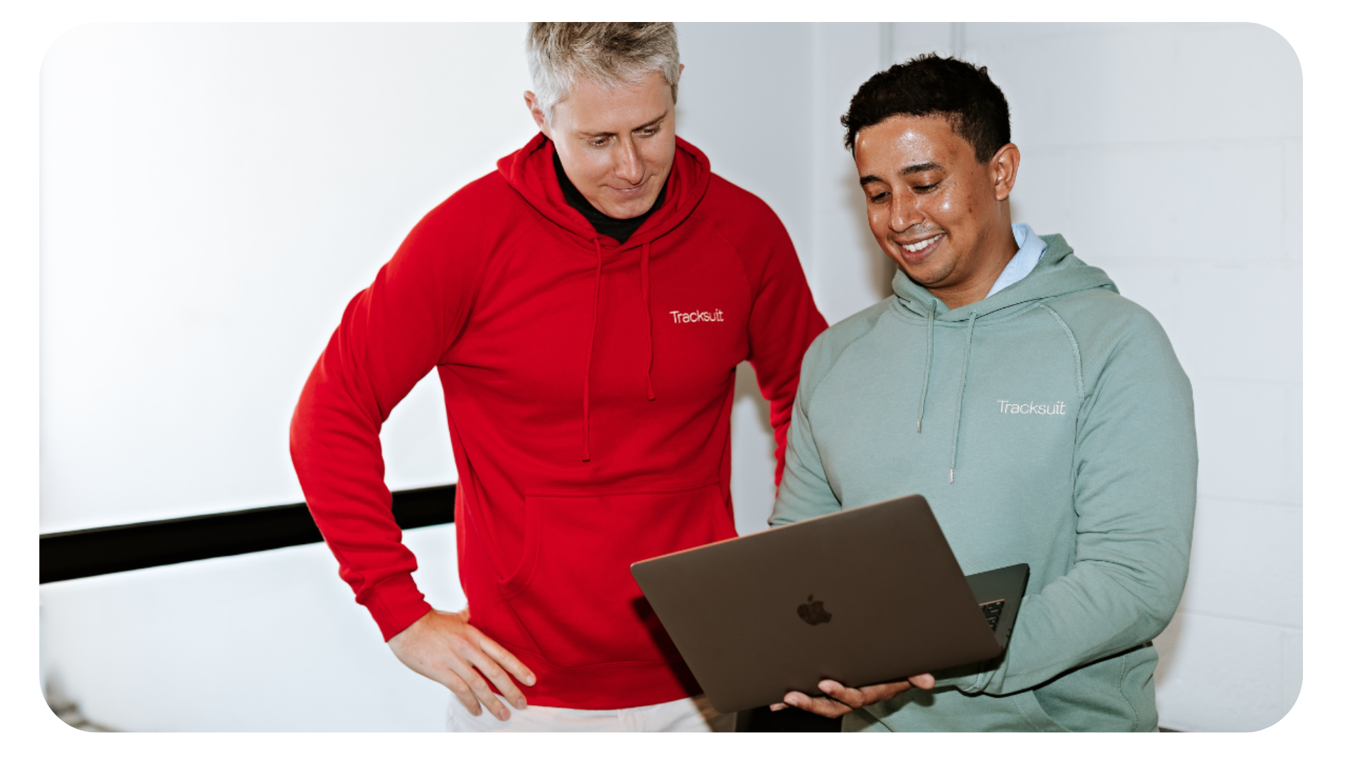 Two men, one wearing a red TechHub hoodie, engaged in a discussion while looking at a laptop screen, symbolizing a collaborative work environment in the tech industry.