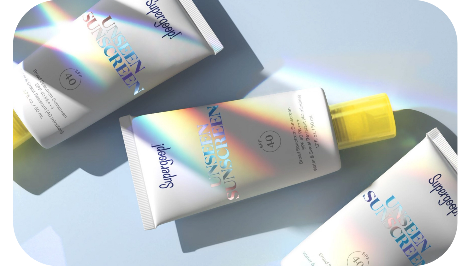 Three bottles of Supergoop! Unseen Sunscreen, a product marketed by AKDM, on a blue surface