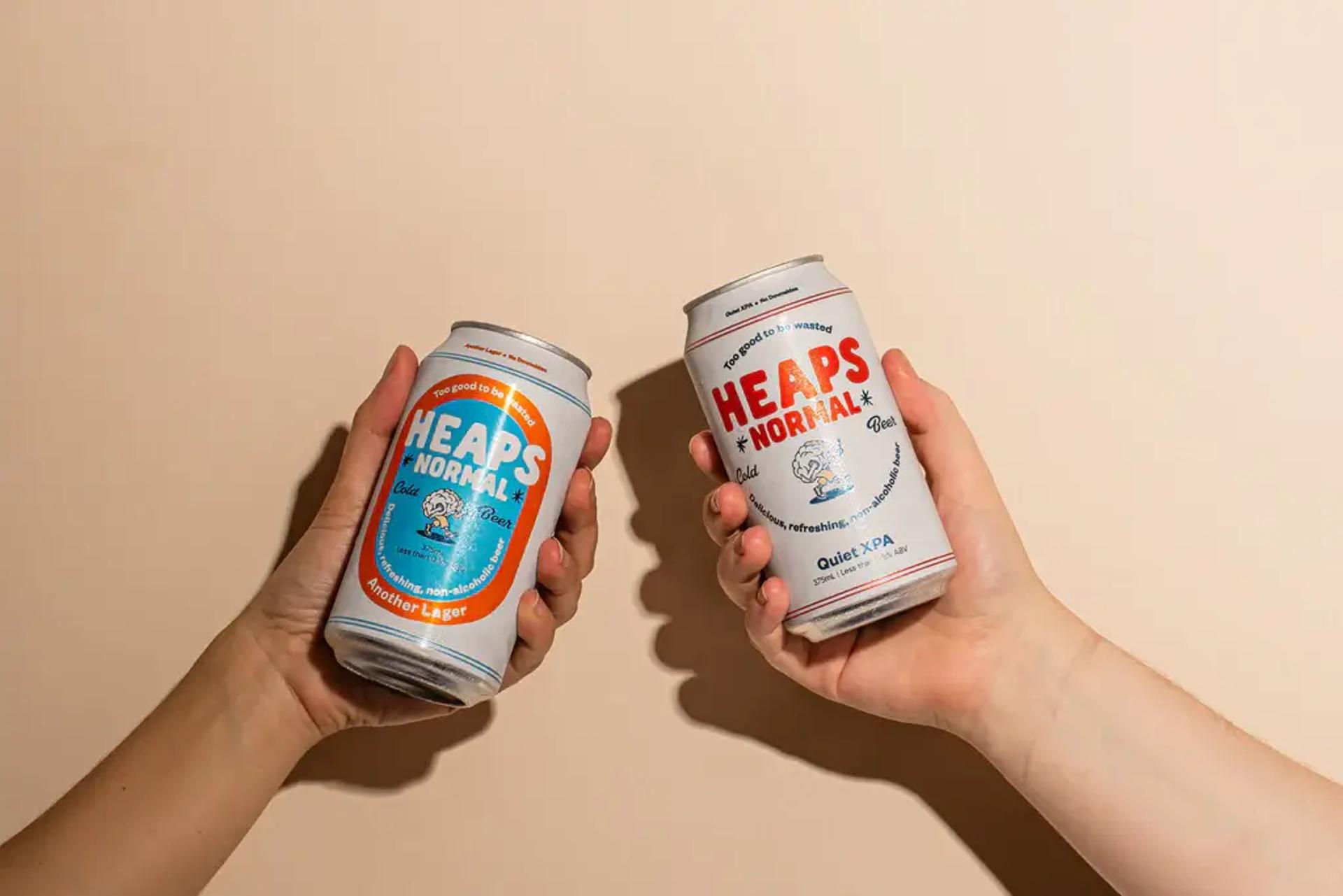 Two people holding Heaps Normal beer cans