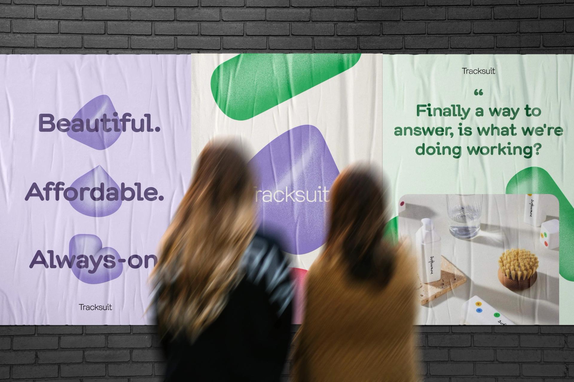 Two women looking at a Tracksuit promotion poster on a brick wall